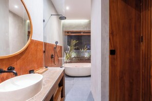 Een moderne badkamer met een groot ovaal wastafel, een ronde spiegel, een douchekop en een bad.