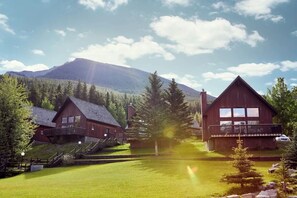 A lodge with a balcony, a mountain backdrop, and a well-maintained lawn. - Beautiful Chalet in the Mountains with Pool and Hot Tubs (Dead Man's Flats)