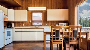 Une cuisine avec des meubles en bois, une table à manger avec des chaises, une fenêtre avec des stores et une vue sur une montagne.