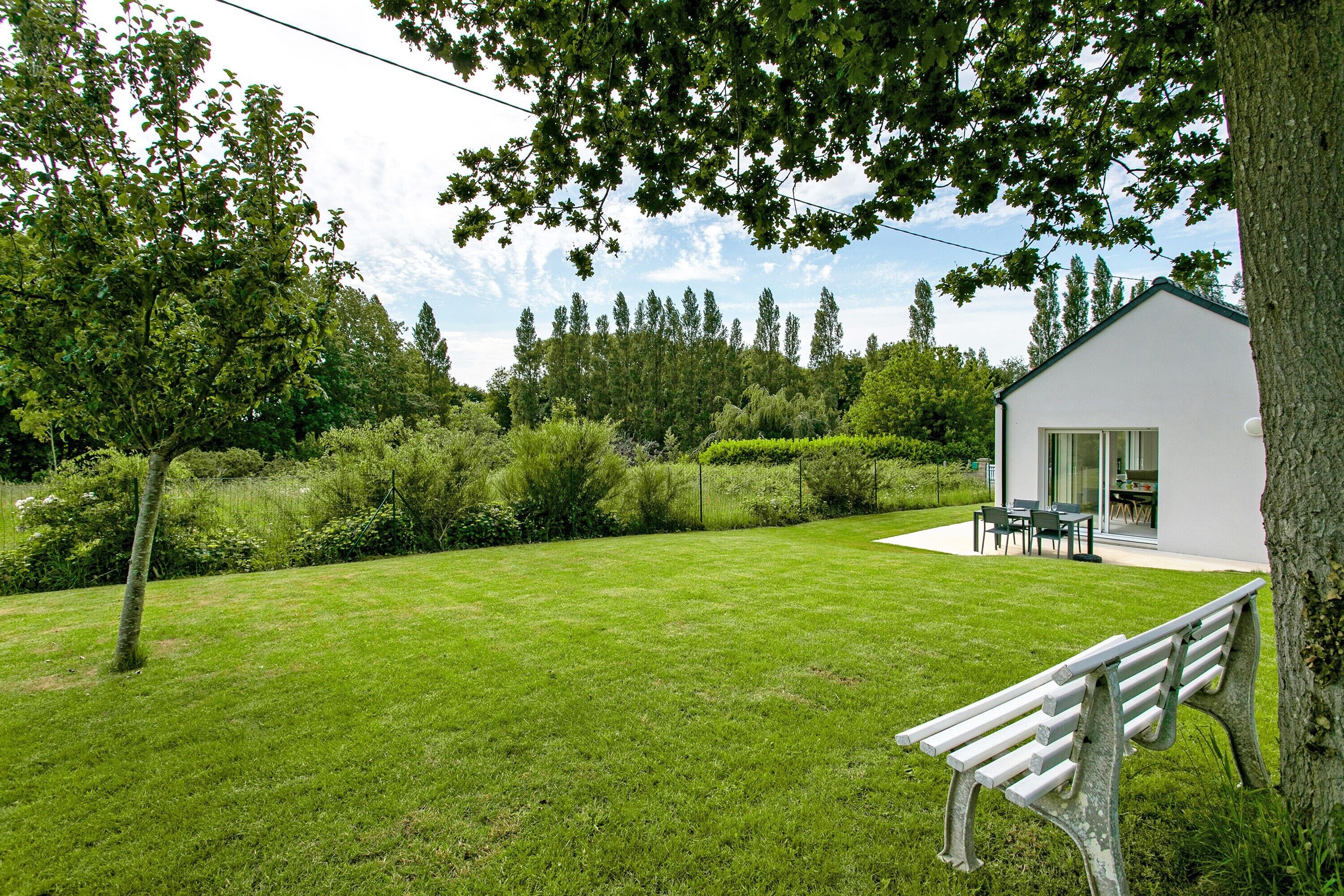 Una casa moderna con un césped cuidado, una banca y un comedor al aire libre con mobiliario.