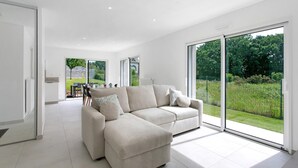 Een moderne woonkamer met een modulaire bank, grote schuifdeuren en uitzicht op een tuin.