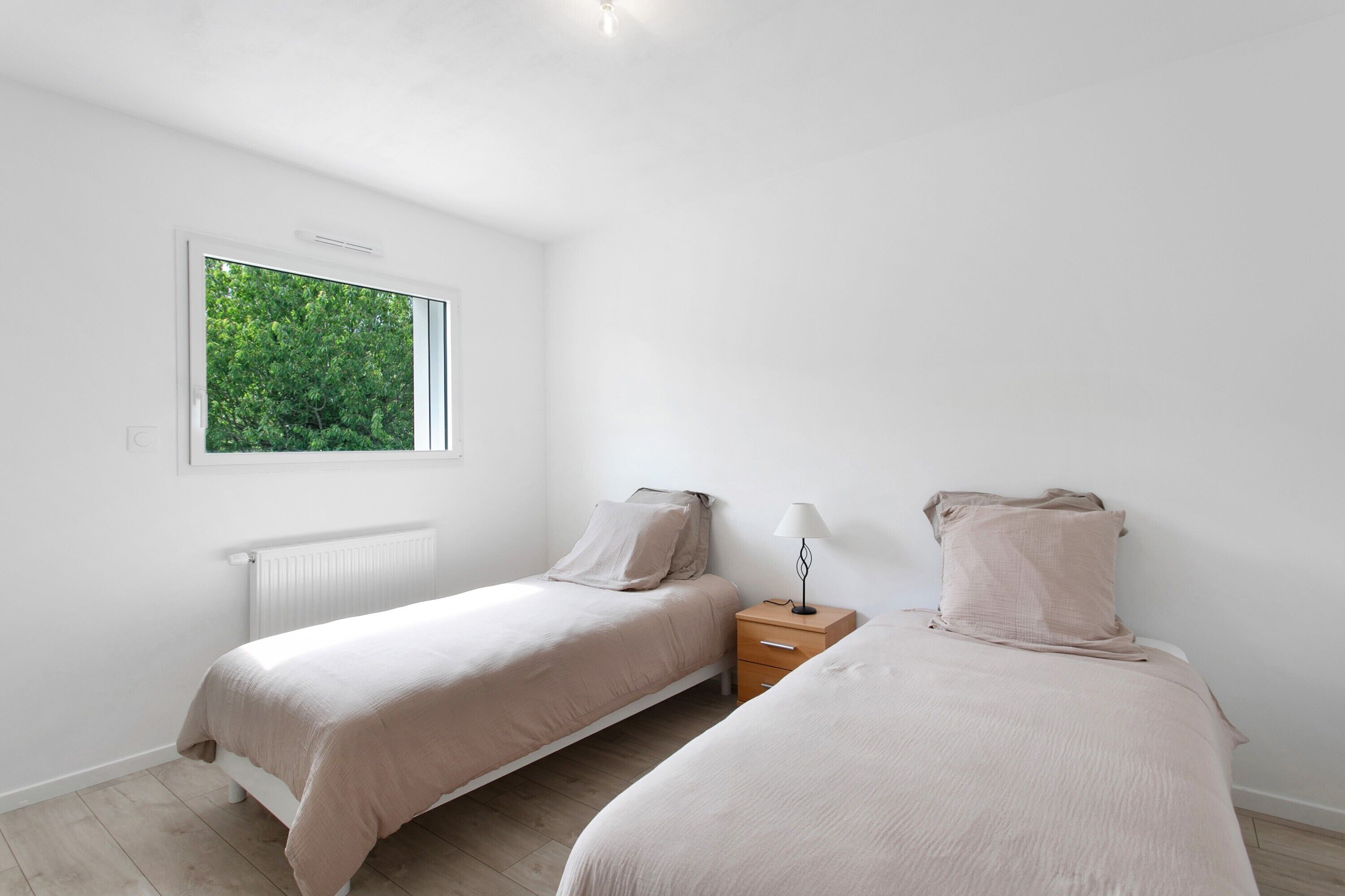 A bedroom with two beds, a window, a radiator, and a nightstand.