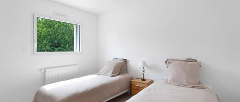 A bedroom with two beds, a window, a radiator, and a nightstand.