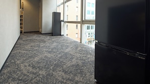 A hallway with carpeted flooring, a refrigerator, and large windows offering a view of buildings outside. - Guesthouse Akasaka2 (Tokyo)
