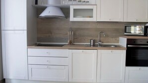 A modern kitchen with white cabinetry, a stainless steel sink, a microwave, and a built-in oven. - Borgo dei Cedri (Bari)