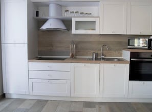 Una cocina moderna con armarios blancos, un lavamanos de acero inoxidable, un microondas y un horno empotrado.