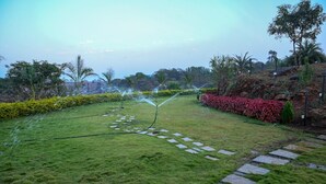 A well-maintained garden with a stone pathway, lush green grass, and various plants. - Bellajooz Lake Resort (Mawal)