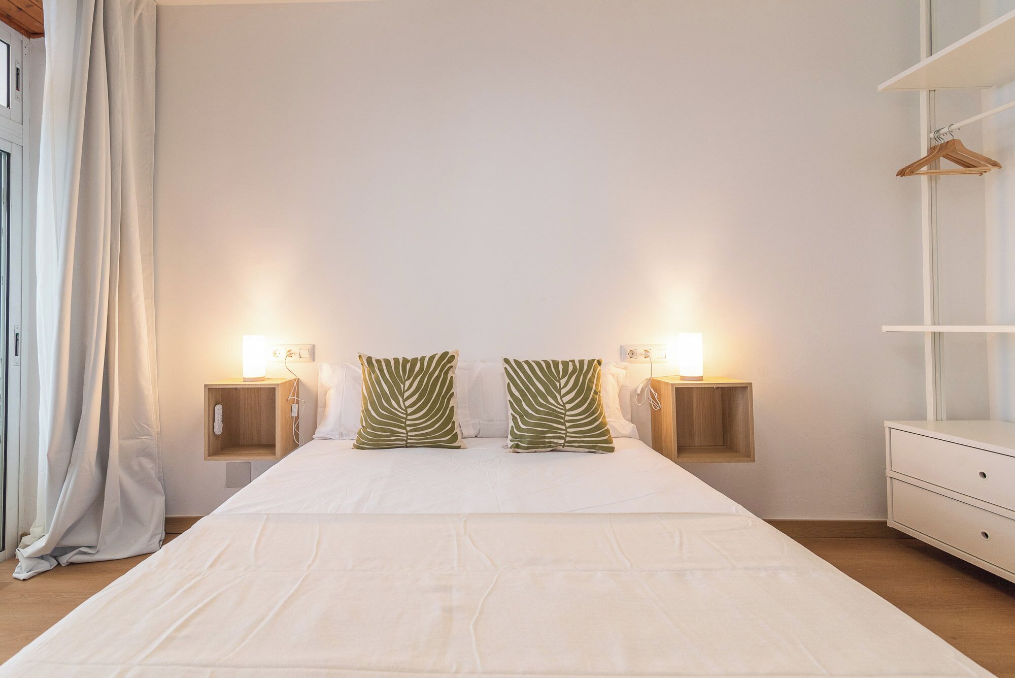 Une chambre avec un grand lit, deux tables de chevet avec des lampes, une armoire et un portant à vêtements.