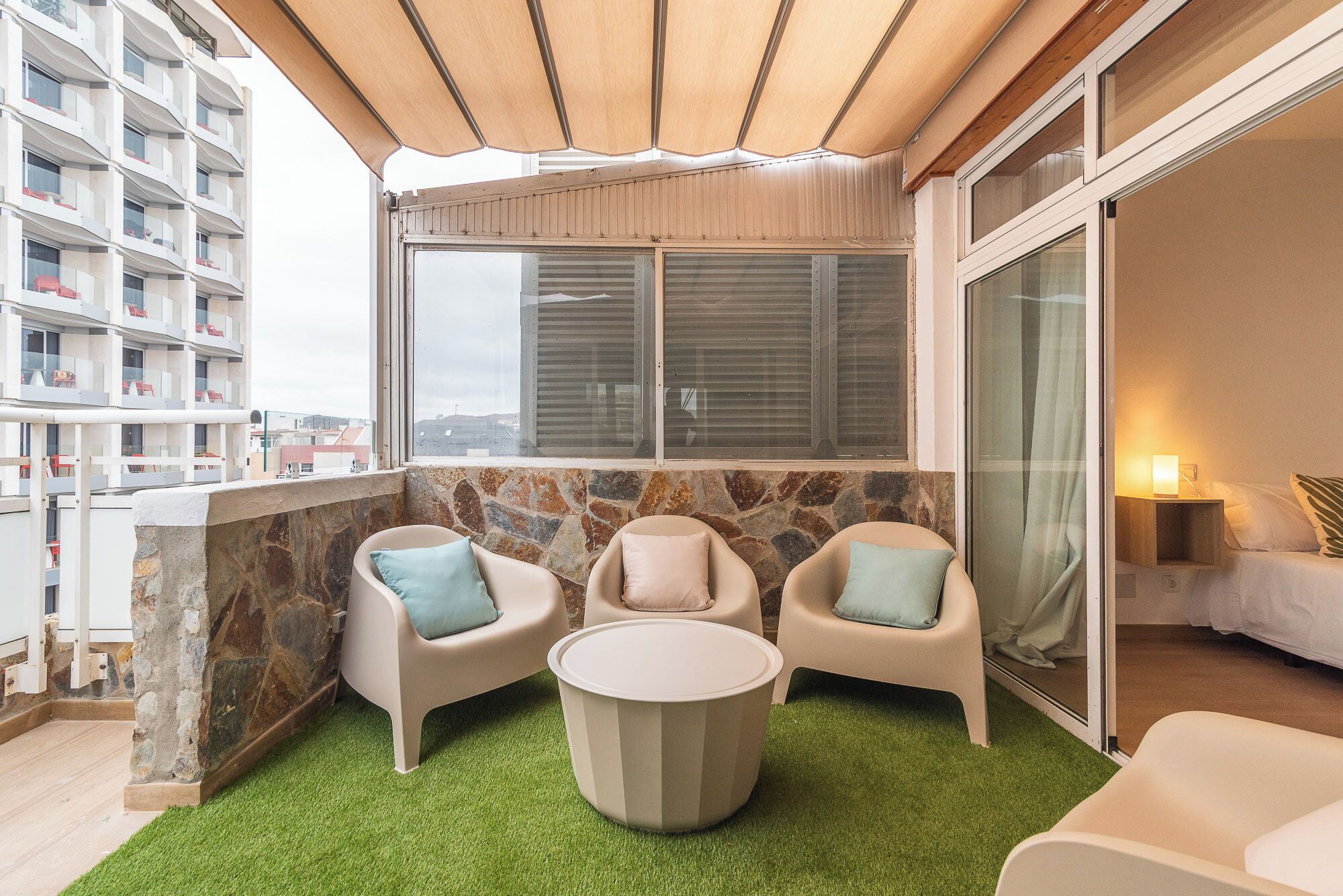 Een balkon met een stenen muur, twee stoelen, een klein rond tafeltje en uitzicht op een gebouw.