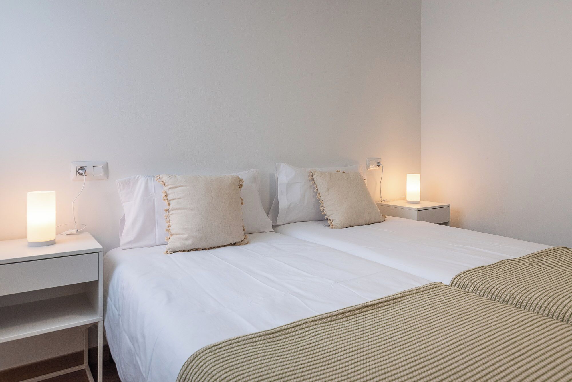 A neatly made bed with white bedding, two bedside lamps, and a bedside table with a lamp.