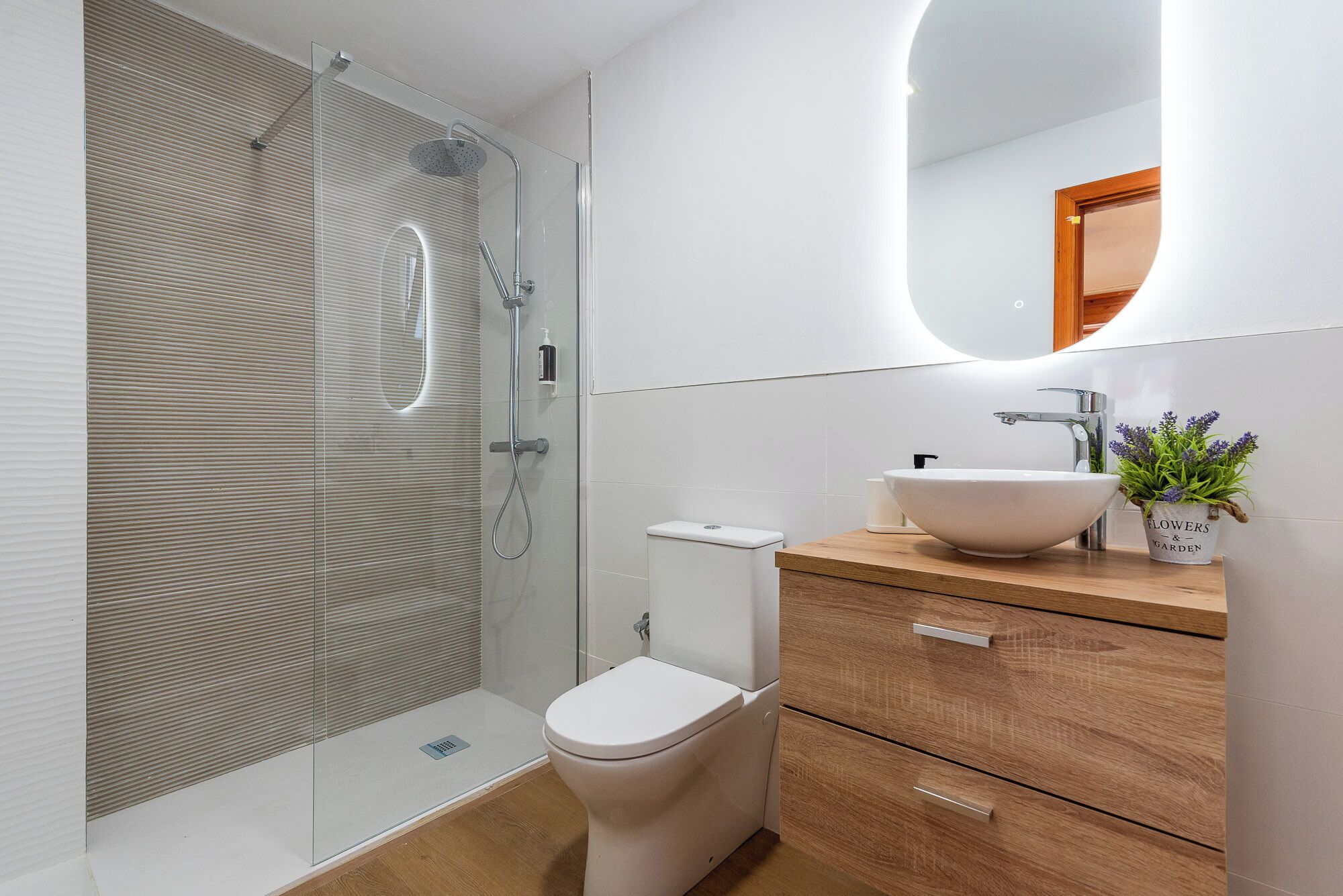 A modern bathroom with a glass shower enclosure, a white toilet, a wooden vanity with a sink, and a mirror.