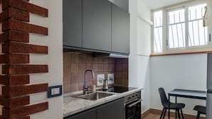 Una cocina compacta con horno integrado, un lavamanos y una ventana con barrotes.