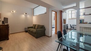 Un salón amplio con una mesa de comedor de vidrio, un sofá verde y un mueble de madera.