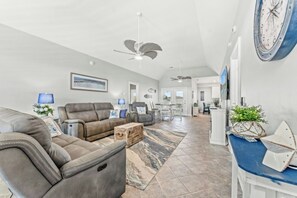Ein großzügiger Wohnbereich mit Sofa, Sesseln, einem Couchtisch und einem Essbereich im Hintergrund.