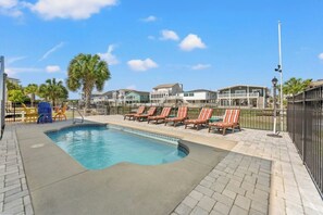Ein Swimmingpool mit Liegestühlen, einer gepflasterten Terrasse und Blick auf Häuser im Hintergrund.