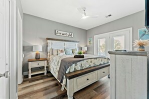 Ein Schlafzimmer mit Bett, Nachttischen, einem Schminktisch und Deckenventilator sowie einem Wandzeichen.