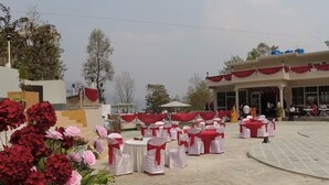 An outdoor event space with round tables and chairs, a stage, and a building in the background.