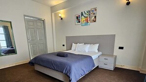 A bedroom with a bed, bedside tables, a nightstand, a door, and wall art.