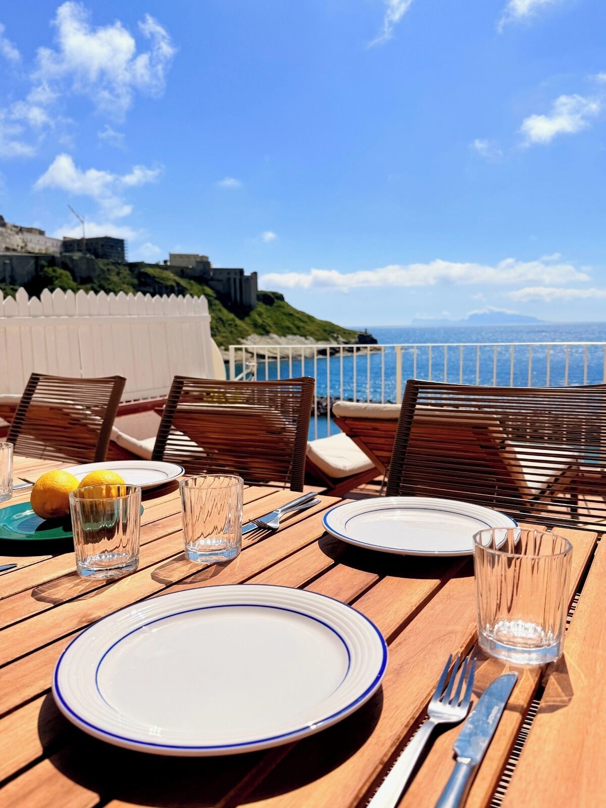 A table set for dining with a view of the sea and a castle in the background.