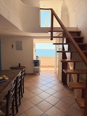 Eine Küche mit Esstisch, Stühlen, einer Holztreppe und Blick aufs Meer.