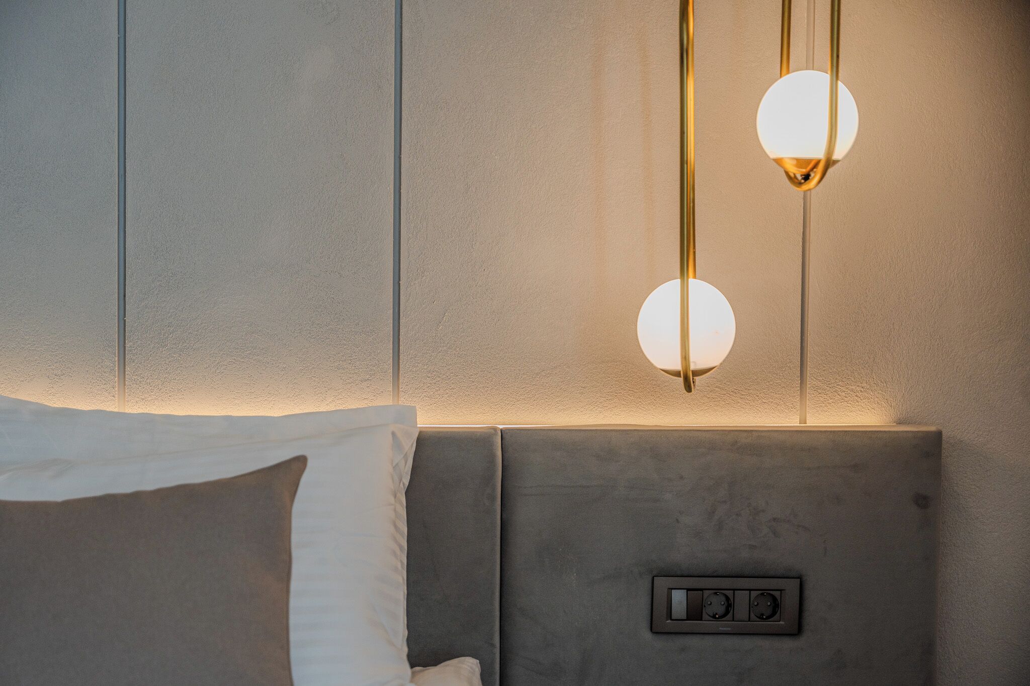 A modern hotel room with a bed, a headboard with control panel, and two pendant lights.