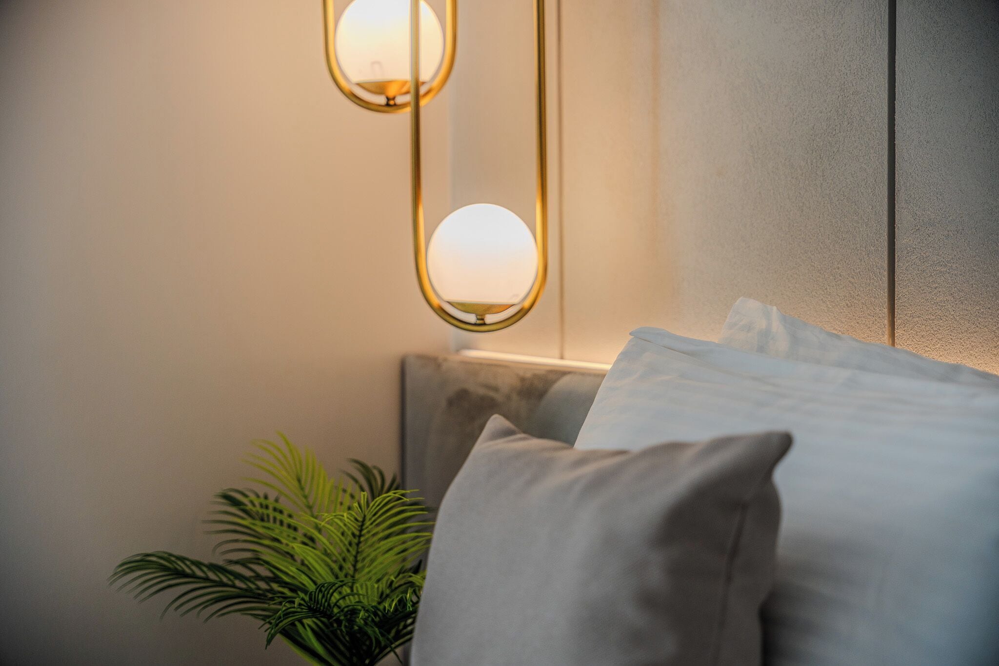 A neatly made bed with pillows, a wall-mounted light fixture, and a potted plant.