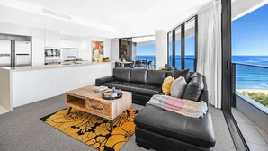 Een moderne woonkamer met een leren zwarte bank, een houten salontafel en uitzicht op de oceaan.