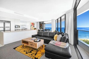 Ein modernes Wohnzimmer mit einem schwarzen Ledersofa, einem Holztisch und Meerblick.