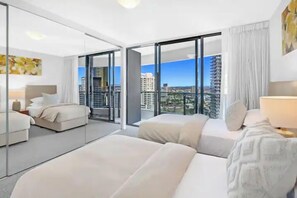 Une chambre d’hôtel moderne, dotée d’un grand lit, d’une table de chevet, d’une lampe et offrant une vue sur le paysage urbain grâce à de grandes fenêtres.