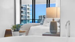 Een hotelkamer met een groot raam, een bed, een nachtkastje met een lamp en een potplant.