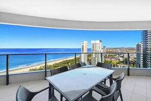 Un balcon avec une table et des chaises en verre, donnant sur une plage et offrant une vue sur la ville.