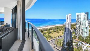 Een balkon met uitzicht op zee en strand, moderne architectuur en een zithoek met een bank.