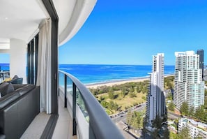 Ein Balkon mit Blick auf den Ozean und Strand, moderne Architektur und eine Sitzecke mit einer Couch.