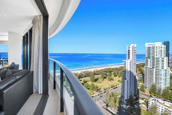 Un balcon avec vue sur l’océan et la plage, une architecture de bâtiment moderne et un coin salon avec un canapé.