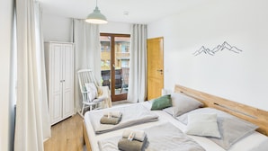 A bedroom with two beds, a wooden headboard, a white ceiling, and a view of a building through a glass door. - Vacation apartment Hüttenzauber for 4 persons, 54 m² (Inzell)