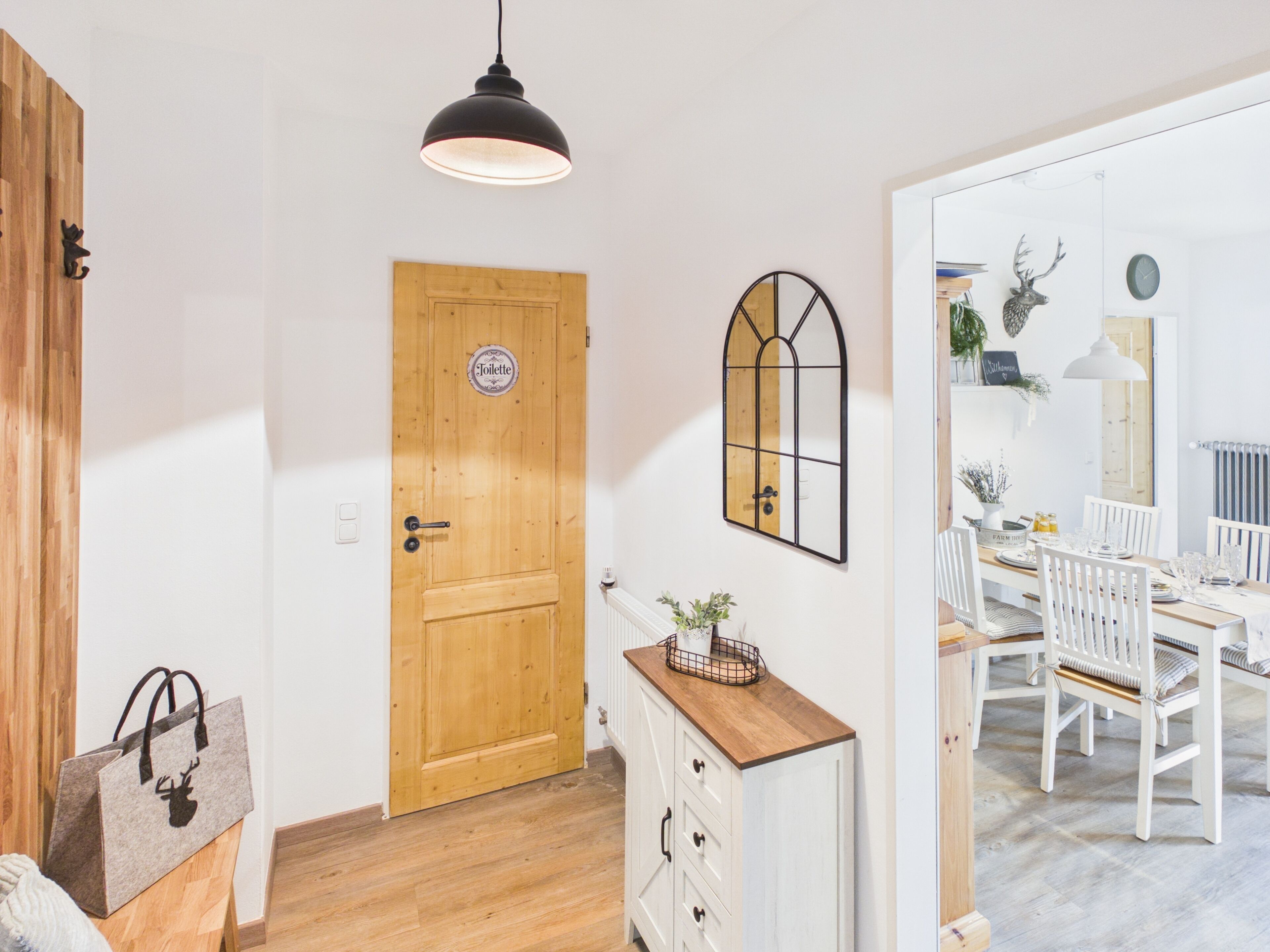 A wooden door with a 'Toilette' sign, a mirror, a white dresser, and a dining area with chairs and a table.