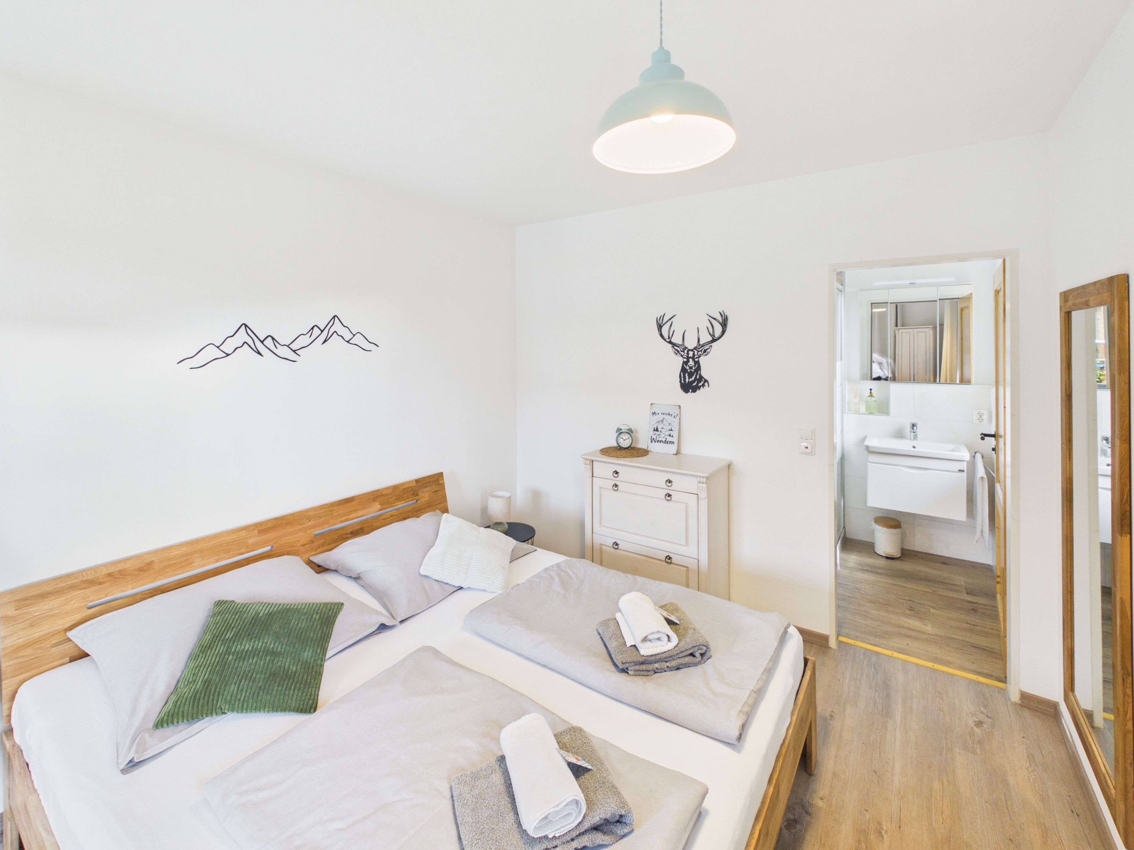 A bedroom with a wooden bed, two pillows, a green throw, and a bedside table with a lamp.