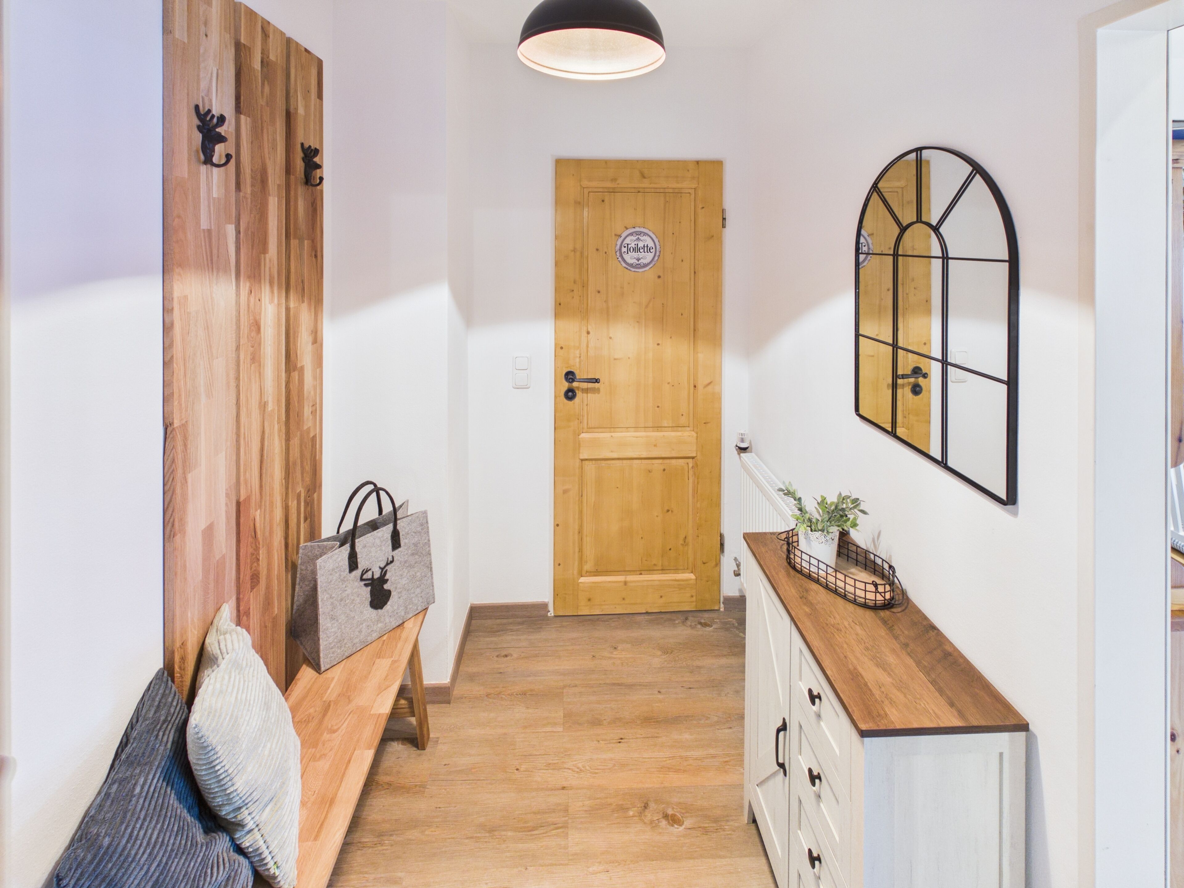 A hallway with a wooden door, a bench with bags, a dresser, and a mirror.