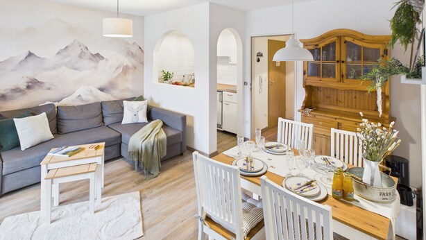 A modern living room with a sofa, dining table set for four, and a kitchen area with wooden cabinets. - Vacation apartment Hüttenzauber for 4 persons, 54 m² (Inzell)