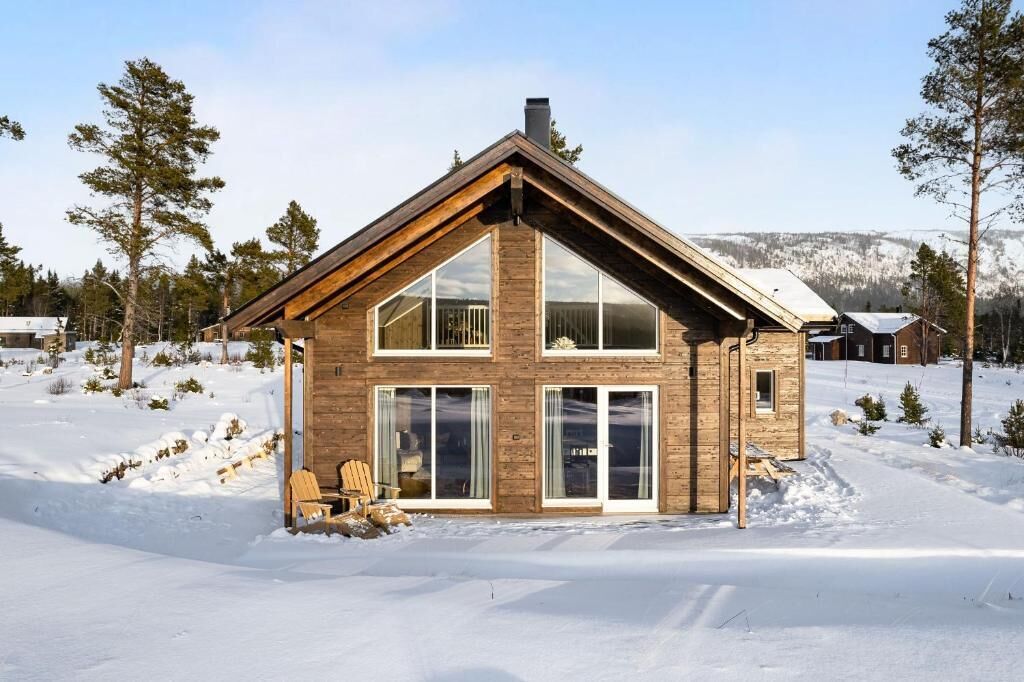 A wooden cabin with large windows, a chimney, and a snow-covered landscape.