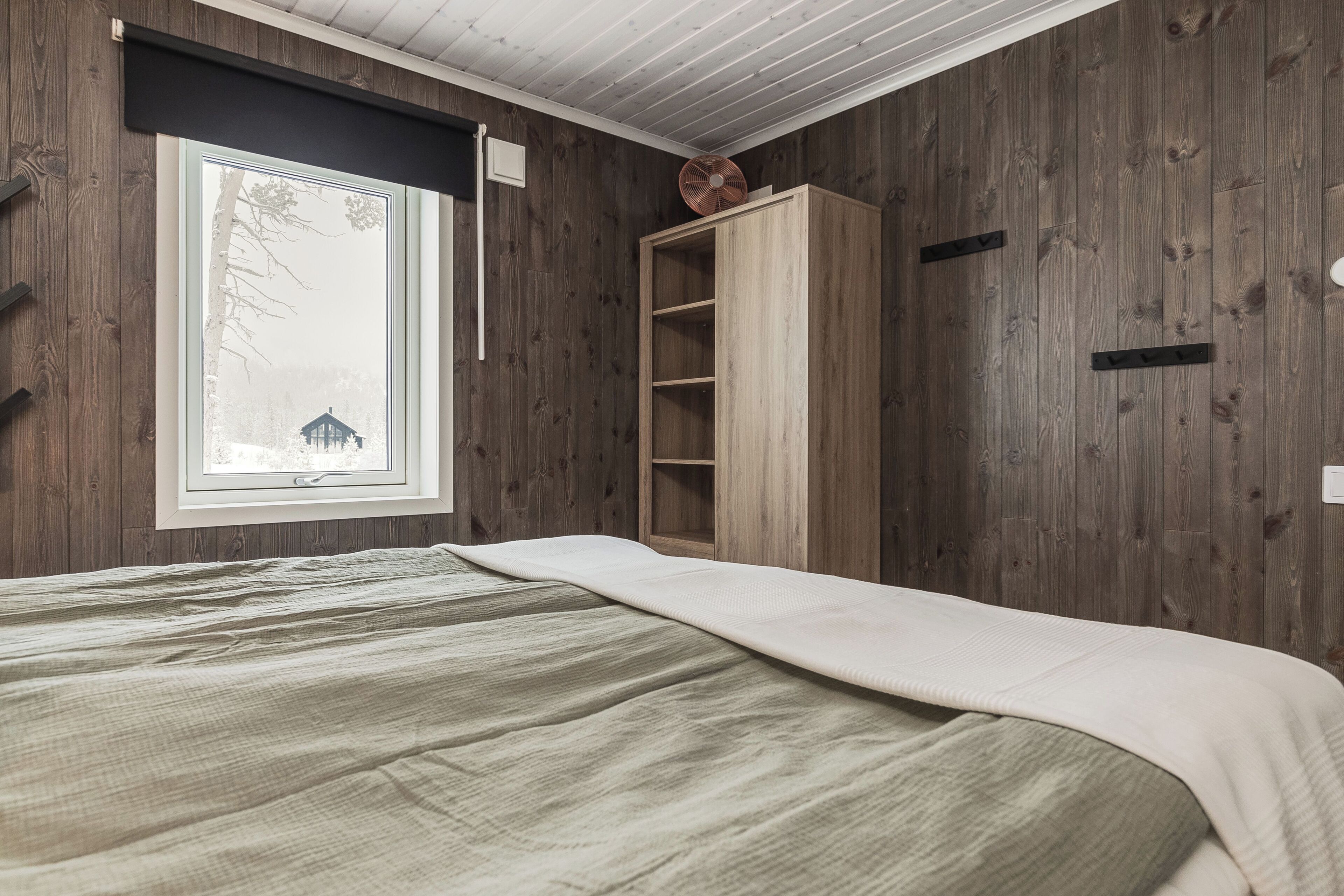 A room with wooden walls, a bed with a white blanket, a window with a view of a traditional building, and a wooden cabinet.