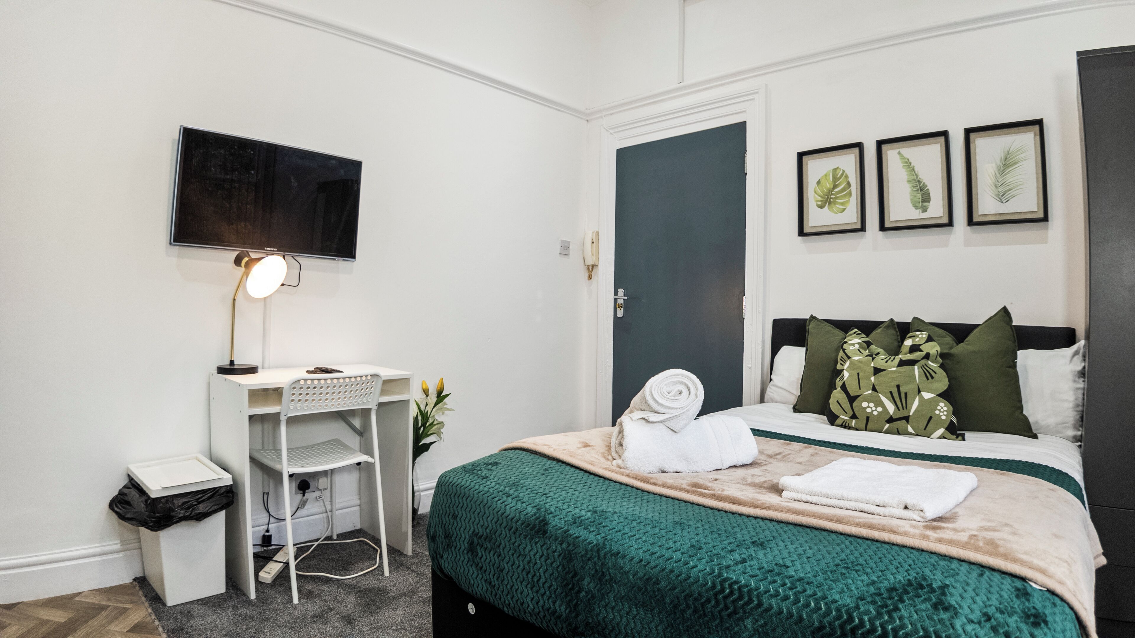 Een hotelkamer met een bed, een bureau, een stoel, een televisie en een deur.