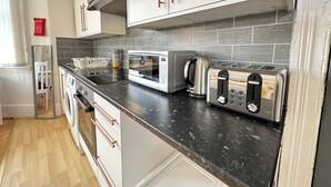 A compact kitchen with a microwave, toaster, kettle, and a coffee maker on the counter. - Modern Retreat in Birmingham (Birmingham)