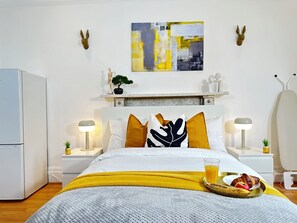 Un dormitorio moderno con una cama, mesitas de noche, una mesita auxiliar, un estante montado en la pared con objetos decorativos y una obra de arte colgada.