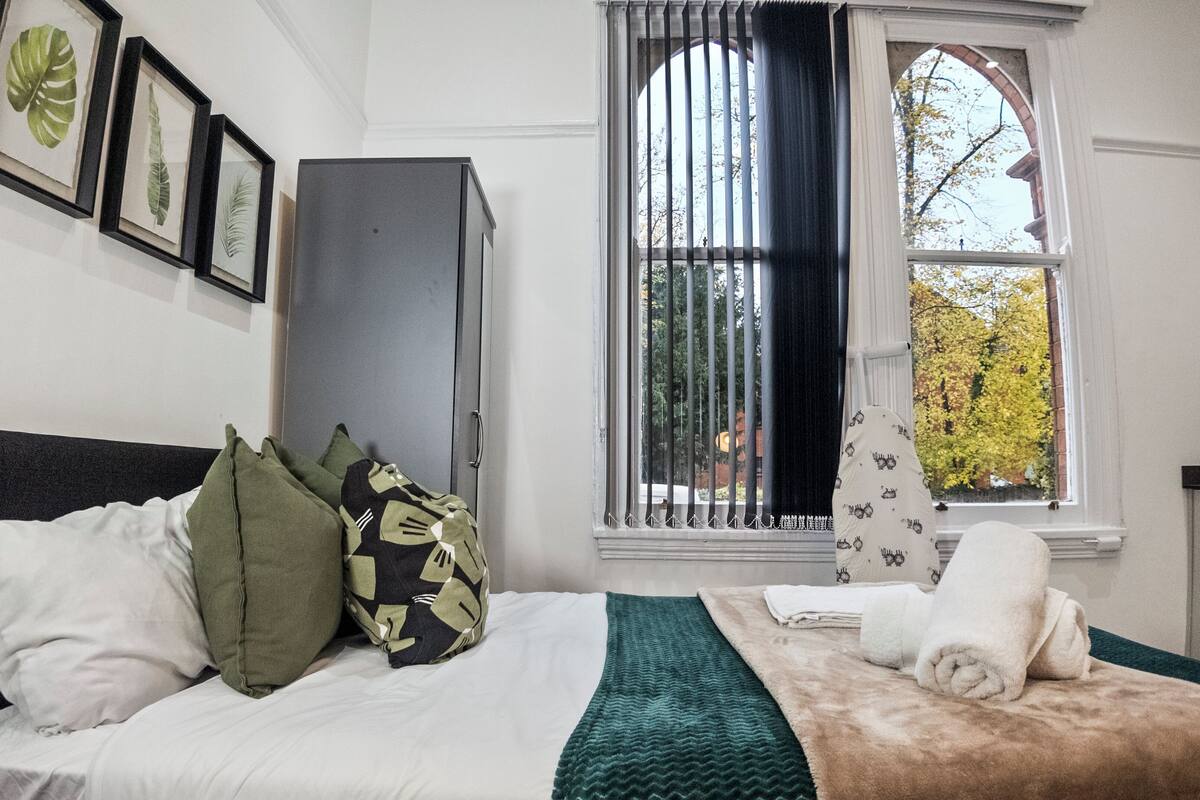 A bedroom with a bed, pillows, a blanket, a wardrobe, and a window with a view.