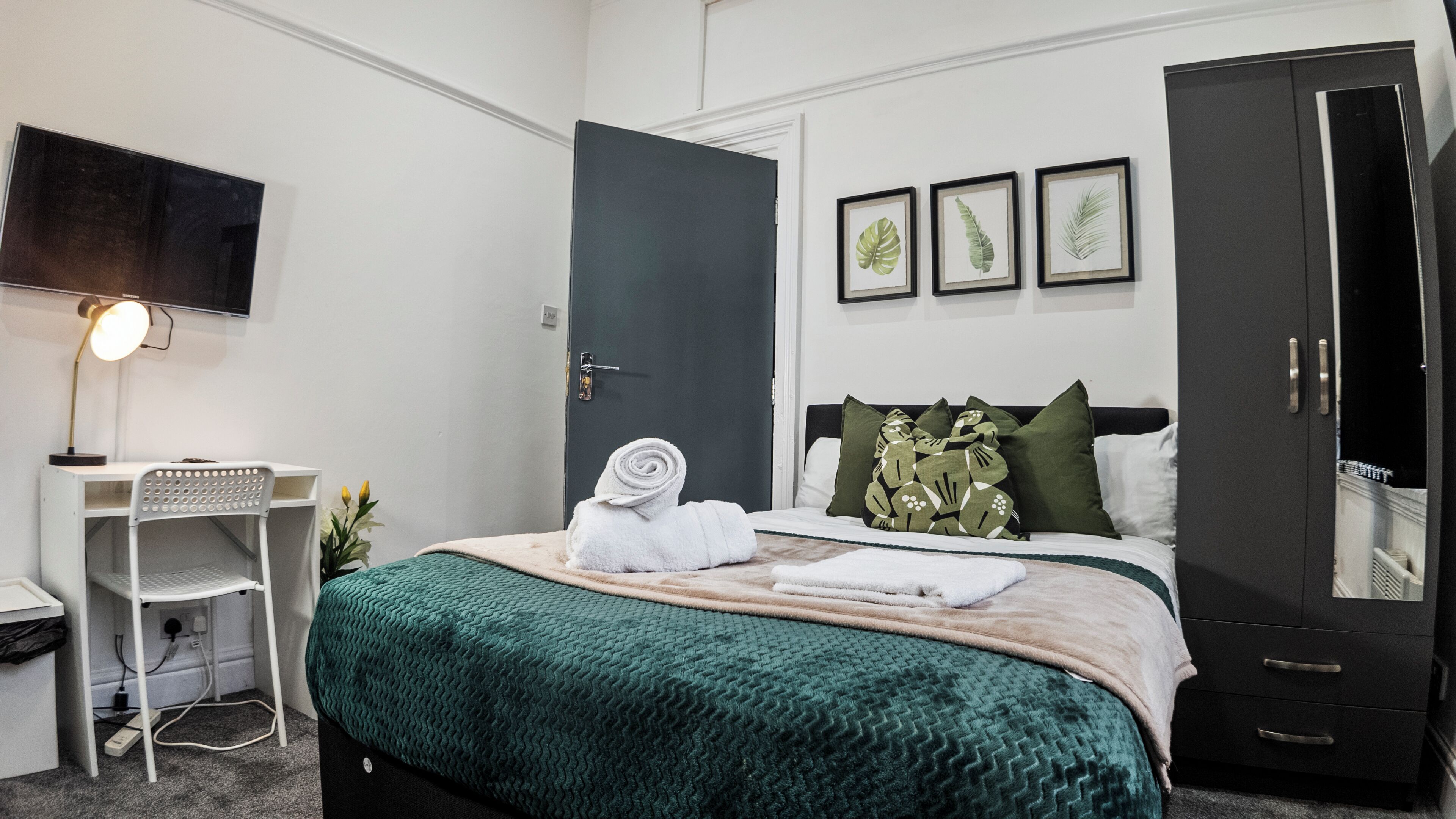Una camera d'albergo con un letto, una scrivania, una sedia, una televisione e un armadio.