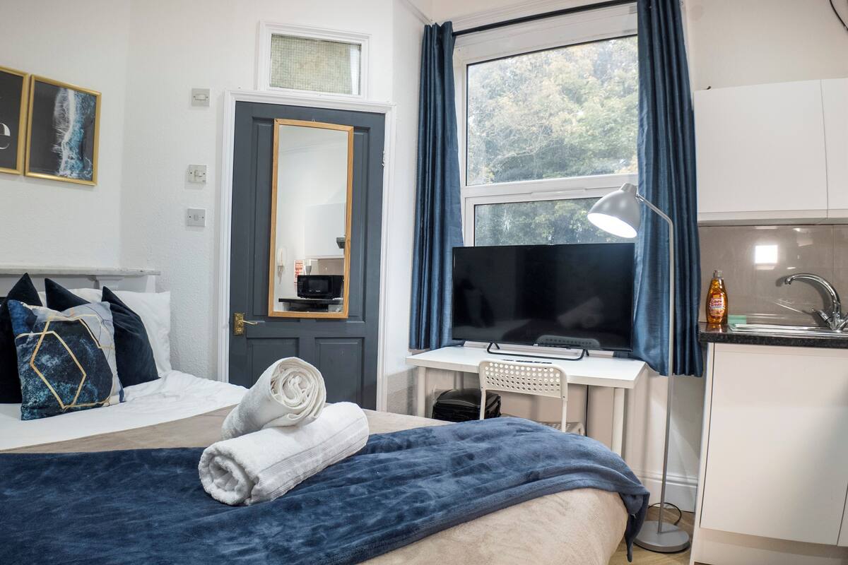 A bedroom with a bed, a desk, a TV, and a window with curtains.