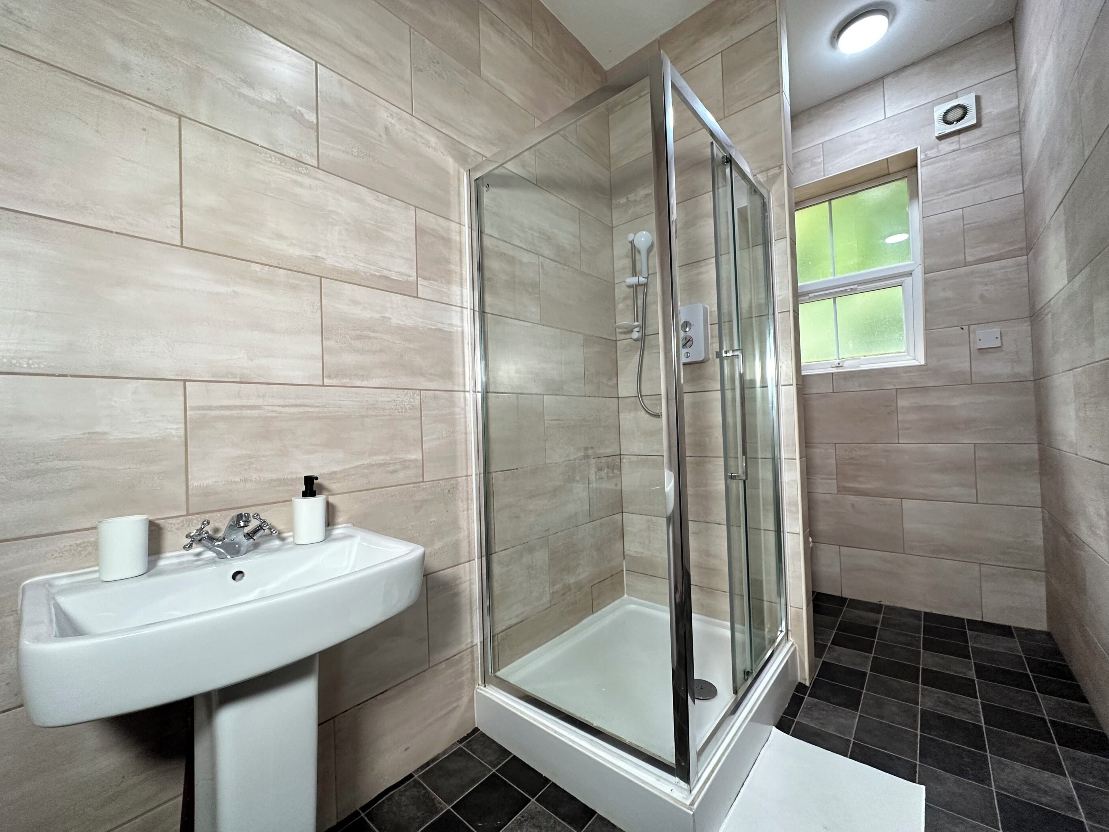 A bathroom with a glass-enclosed shower, a sink, and a window.