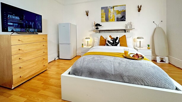A modern hotel room with a bed, a television, a wardrobe, a small refrigerator, and a bedside table with a lamp. - Modern Retreat in Birmingham (Birmingham)
