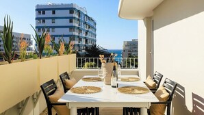 A balcony with a white table set for four, surrounded by black chairs with beige cushions, a vase with flowers, and a bottle of wine. - Magic on Main (Cape Town)